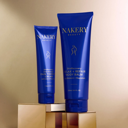 Two blue tubes of Nakery Beauty products on a gold stand with a beige background