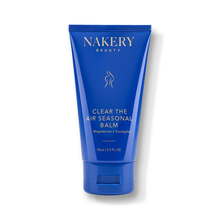 A blue squeeze tube of NAKERY BEAUTY Clear The Air Seasonal Balm, featuring white text and a small white line-art graphic of a face and neck, set against a clean white background with a soft shadow.
