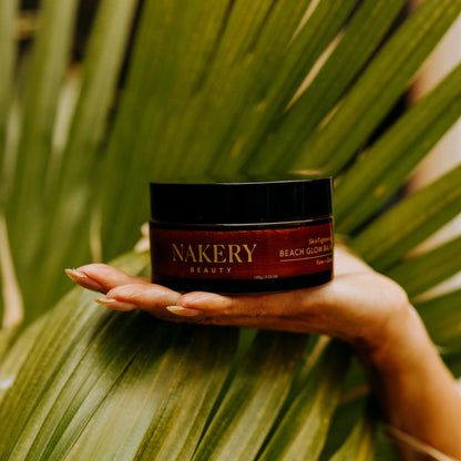 Hand holding a jar of Beach Glow Balm against a leafy background
